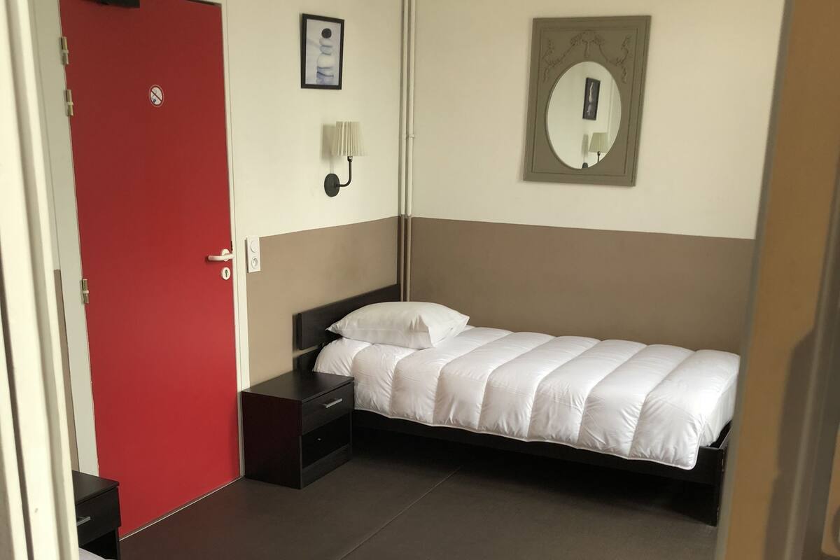 A hotel room with two beds, a red door, a wall-mounted lamp, and a mirror.