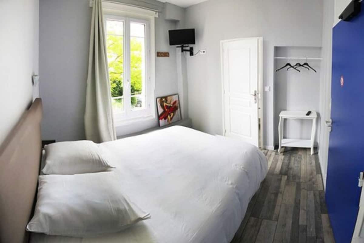 A bedroom with a bed, a television, a window with curtains, a door, and a coat rack.