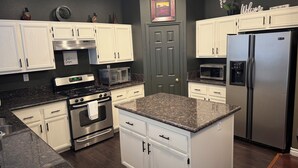 A modern kitchen with white cabinets, stainless steel appliances, granite countertops, and a dark wall. - Best Kept Secret! 4 King Beds ·Hot Tub · 9ft Pool Table · 5 Min to South Point (Las Vegas)
