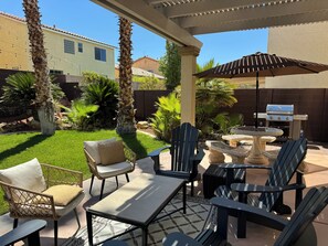 An outdoor patio area with a grill, chairs, and a table. - Best Kept Secret! 4 King Beds ·Hot Tub · 9ft Pool Table · 5 Min to South Point (Las Vegas)