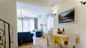 A dining area with a table set for two, a blue sofa in the background, and a painting on the wall.