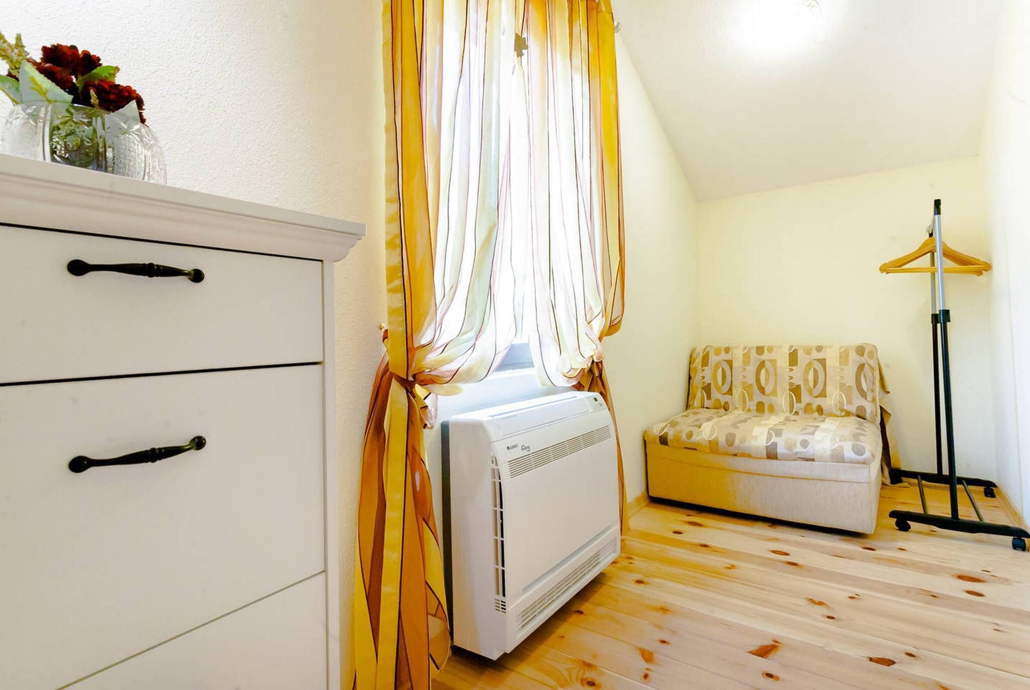 Une pièce avec une commode blanche, un radiateur, un canapé à motifs et un porte-manteau sur pied.