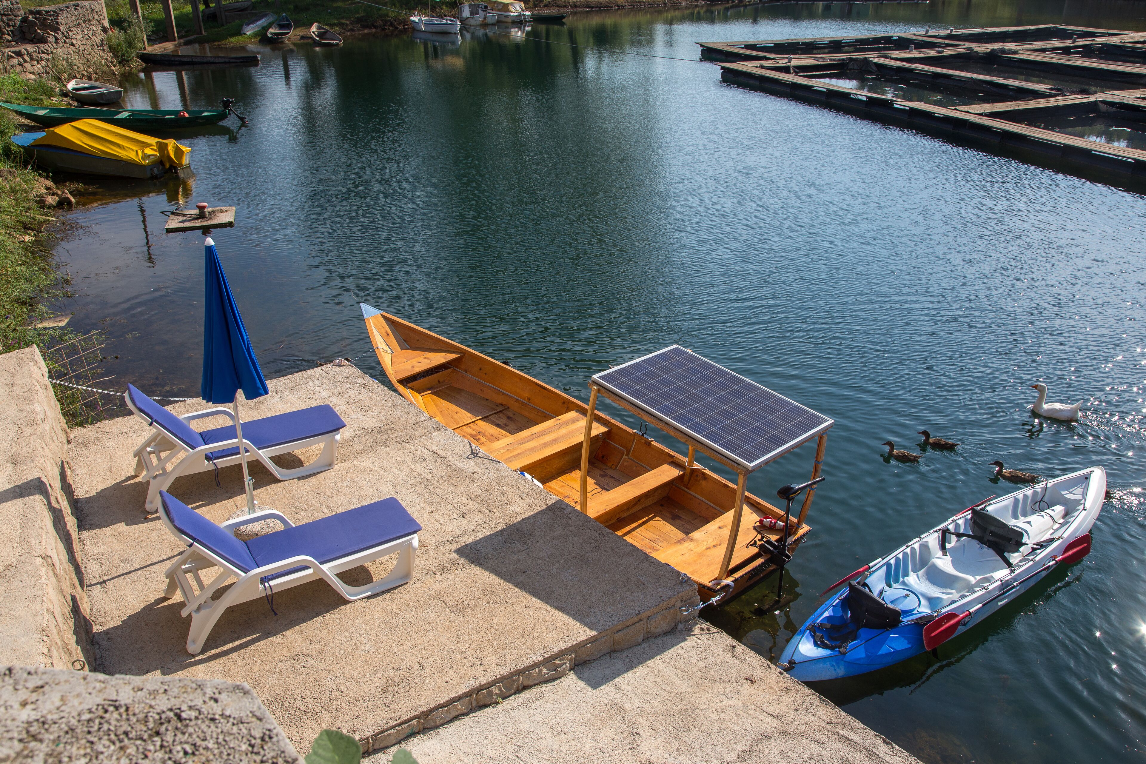 Een steiger met een klein bootje, lounge stoelen en een zonnepaneel.