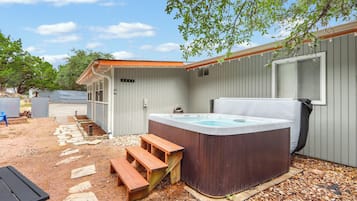 Een hottub met houten trap, een overdekte patio en een metalen hek in een achtertuin.