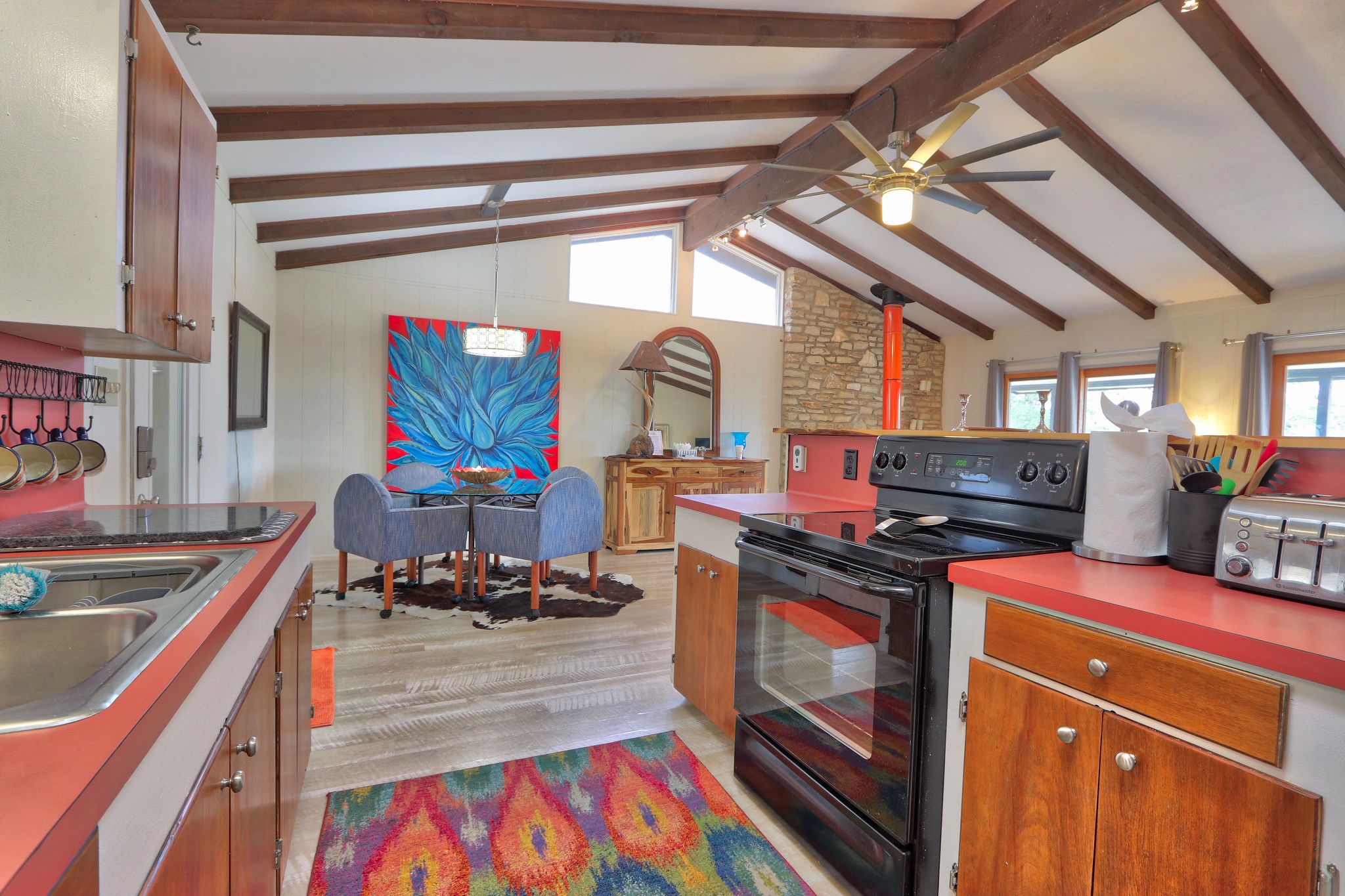 A kitchen with wooden cabinets, a red countertop, a stove, and a dining area with a table and chairs.