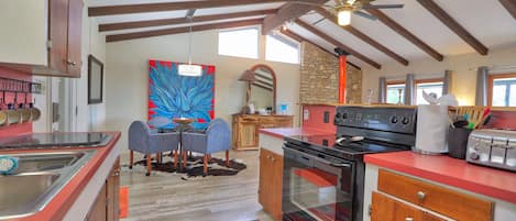 A kitchen with wooden cabinets, a red countertop, a stove, and a dining area with a table and chairs.
