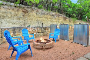 A fire pit with chairs and a stone wall in the background.