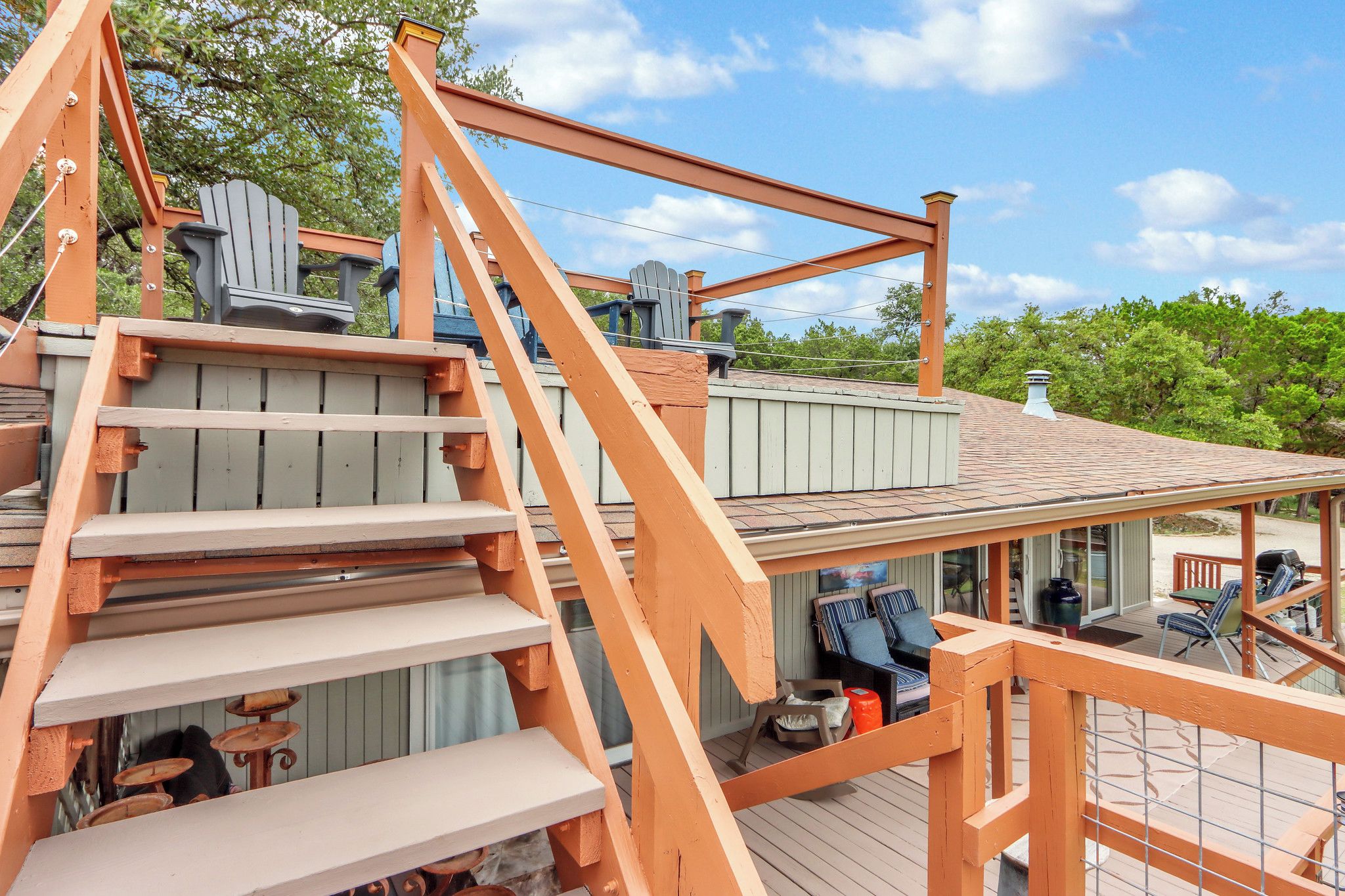Eine Holzterrasse mit einer Treppe zu einem überdachten Bereich, der Adirondack-Stühle und einen Grillplatz bietet.