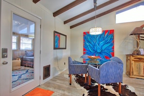 A dining area with a glass table and blue upholstered chairs, a large abstract painting, and a wooden cabinet with a lamp. - Close to town - Amazing Views - Pet Friendly house in Wimberley! (Wimberley)