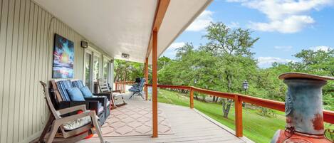 A covered porch with rocking chairs, a fire pit, and a view of a green landscape.