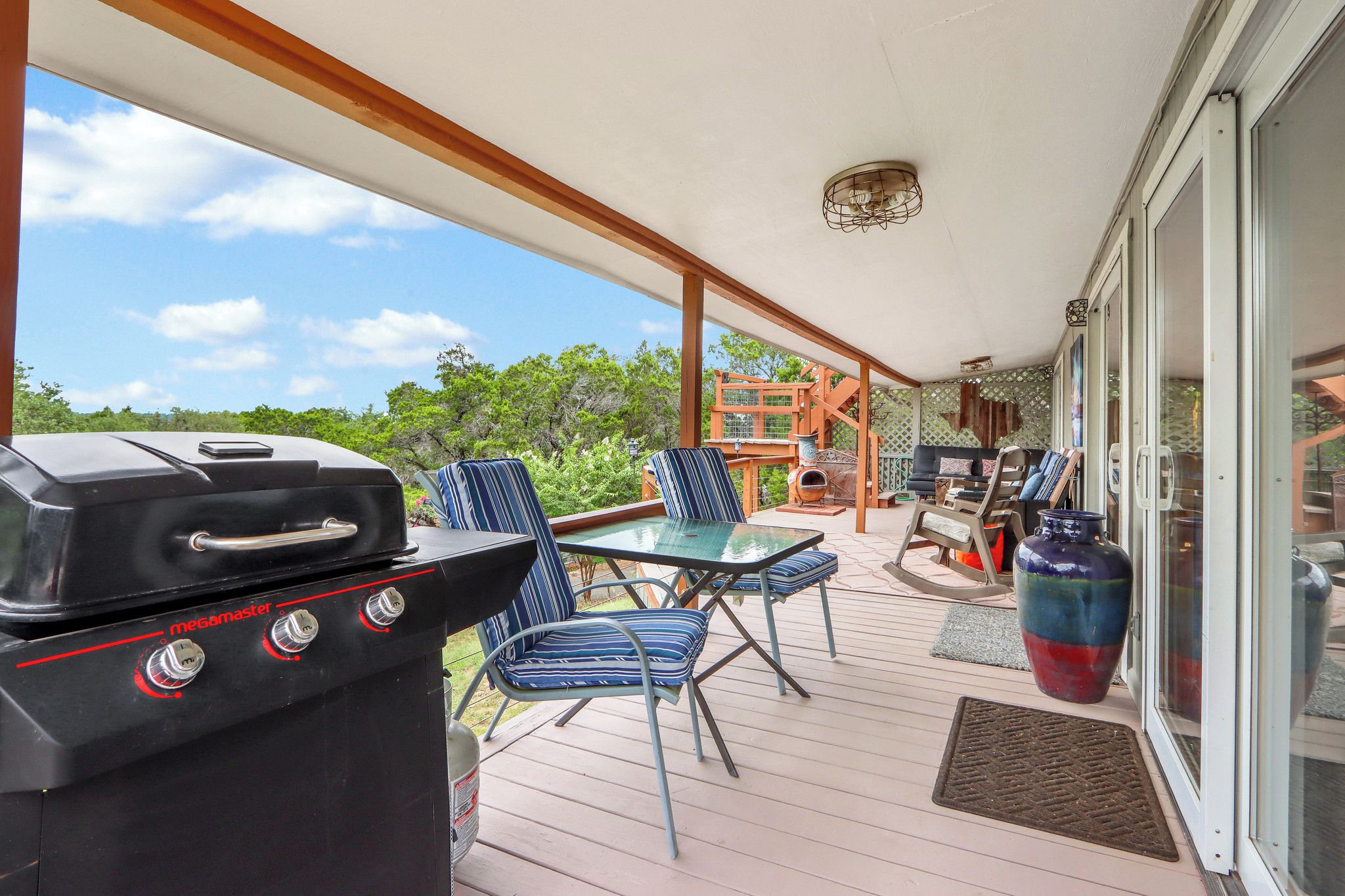 Un espace extérieur abrité, équipé d’un barbecue, de sièges et offrant une vue sur la verdure environnante.