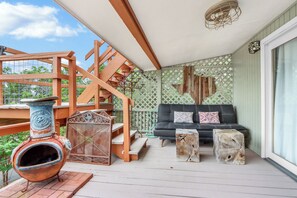 A covered outdoor area with a wooden staircase, a black sofa with patterned cushions, and rustic decor including a ceramic pot and wooden stools. - Close to town - Amazing Views - Pet Friendly house in Wimberley! (Wimberley)