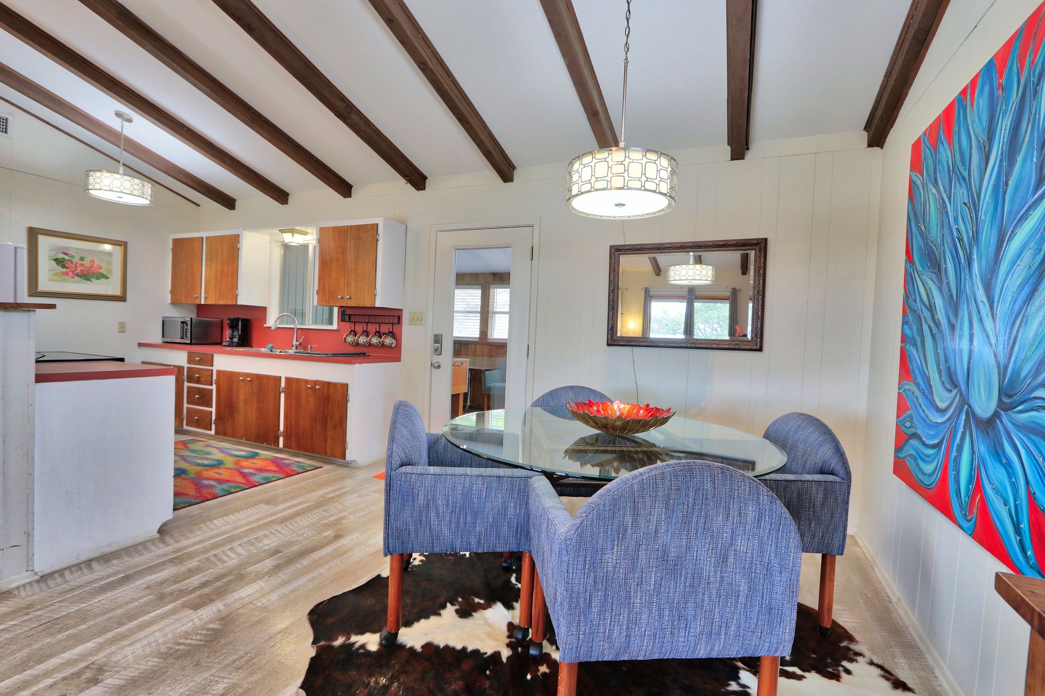 A modern kitchen with wooden cabinets, a microwave, and a dining area with a glass table and blue chairs.