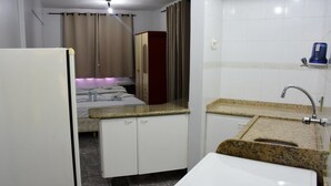 A compact hotel room with a kitchenette, a bed with a headboard, a wardrobe, and a bathroom with a sink and mirror. - ADTUR CTC Condomínio Golden (Caldas Novas)