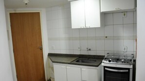 A small kitchen with white cabinets, a wooden door, a granite countertop, a sink, and a gas stove. - ADTUR CTC Condomínio Golden (Caldas Novas)