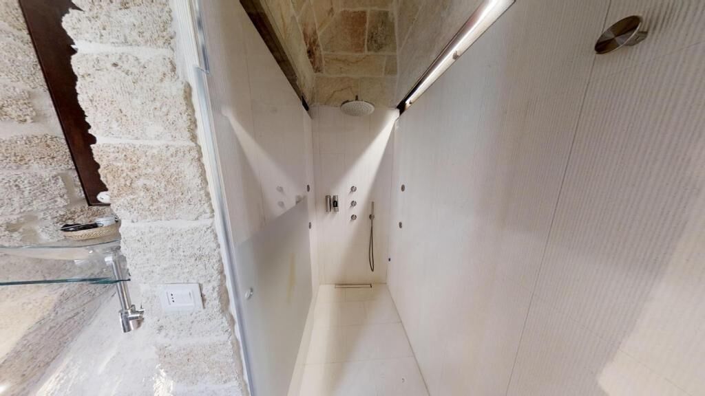 Une petite salle de bain aux murs blancs, dotée d’une douche en verre et d’un mur d’accent en pierre.