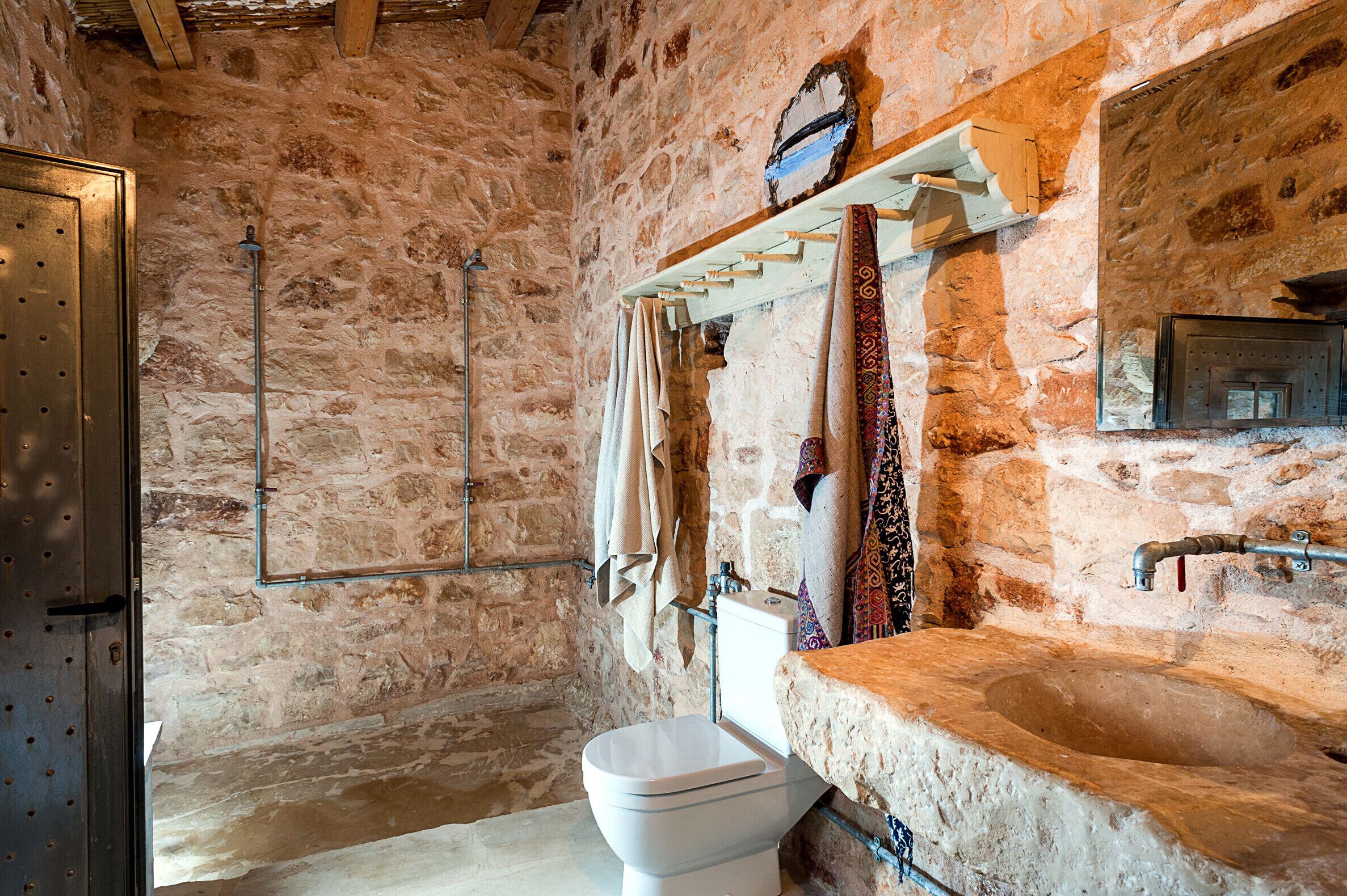 Un bagno rustico con parete in pietra, uno scaffale di legno con asciugamani, un water bianco e un lavabo in pietra.