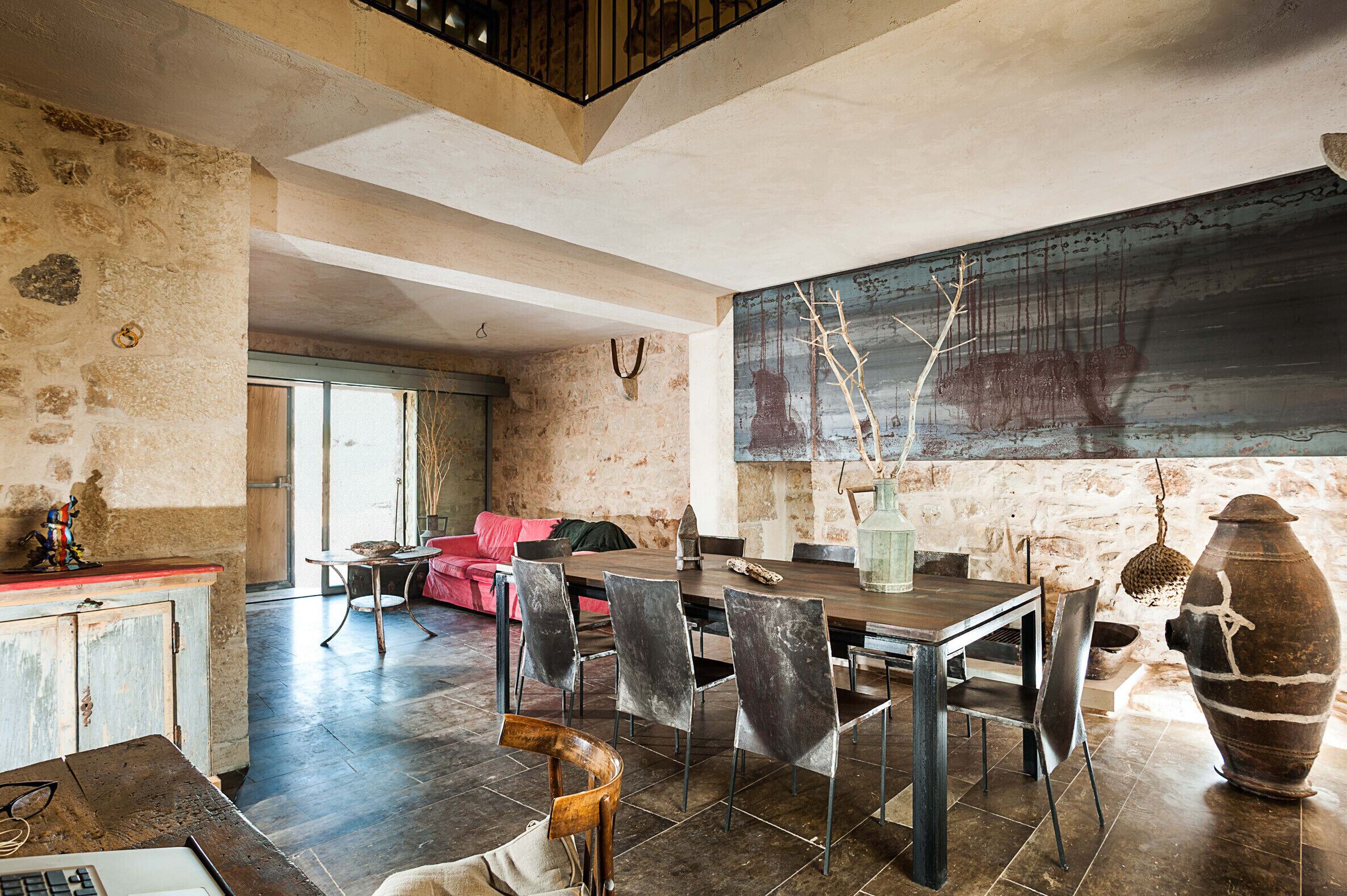A spacious dining area with a large table and chairs, a rustic stone wall, and a large abstract painting.