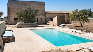 A pool area with a stone building, outdoor seating, and a clear blue pool. - Exclusive villa with private pool in Ragusa, DiCasaInSicilia (Santa Croce Camerina)