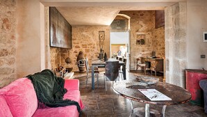 A rustic interior with a stone wall, a pink sofa, a round table, and a dining area with chairs and a laptop. - Exclusive villa with private pool in Ragusa, DiCasaInSicilia (Santa Croce Camerina)