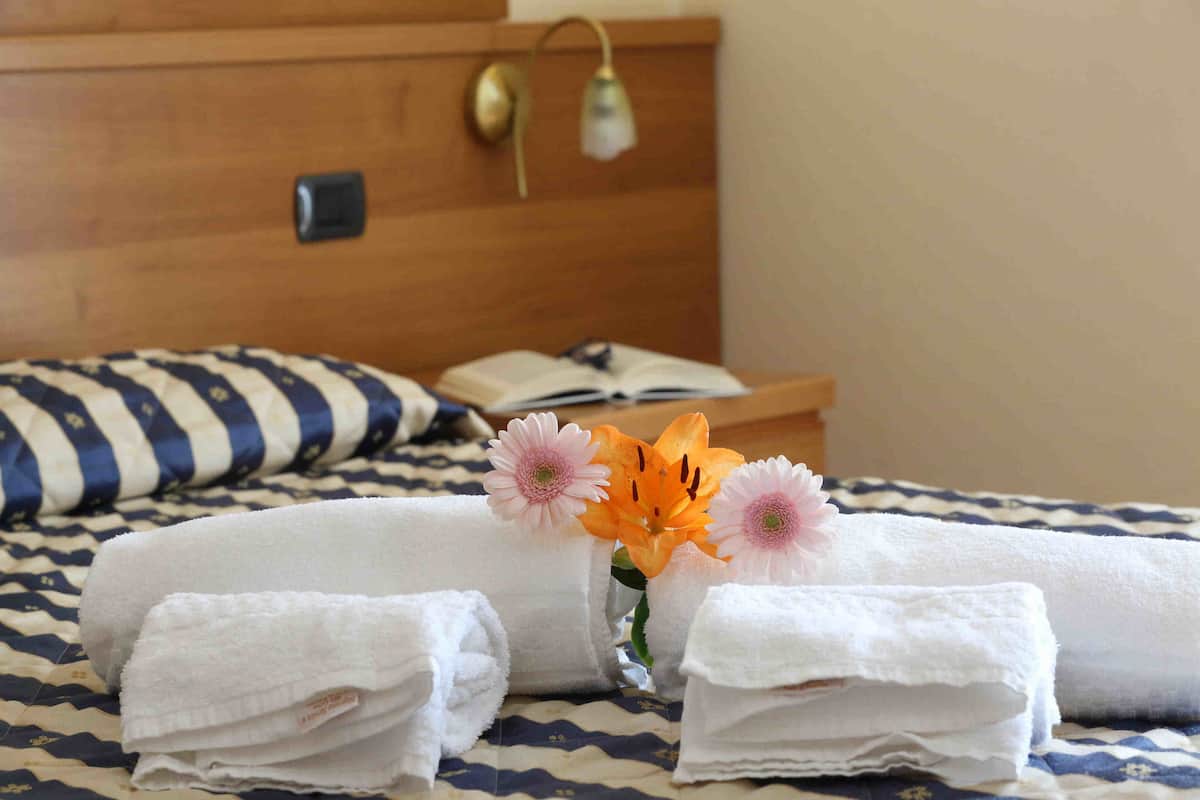 Ein ordentlich bezogenes Bett mit gefalteten Handtüchern und zwei Blumen in einer Vase.
