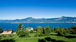 Une vue pittoresque d’un lac, avec des montagnes en arrière-plan et une maison avec un jardin au premier plan.
