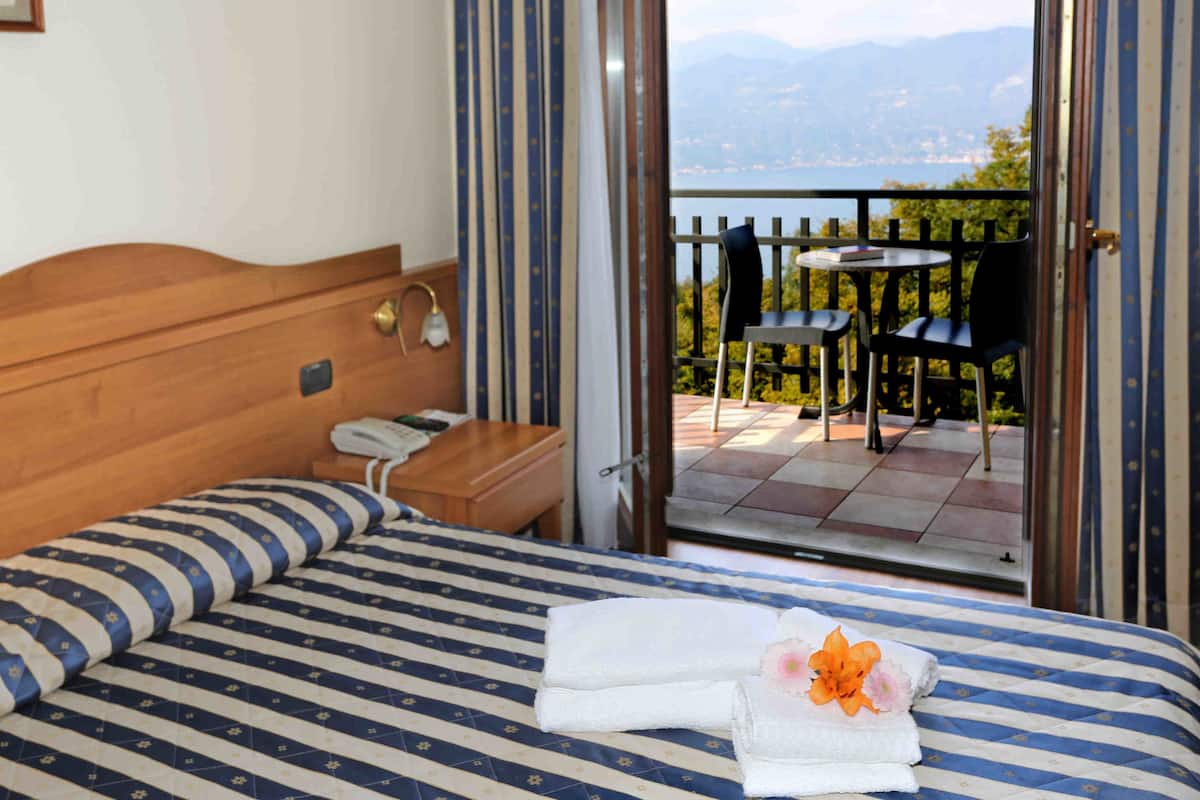 Ein Hotelzimmer mit Bett, Nachttisch mit Telefon und Blick auf einen Balkon mit Stühlen und Tisch.