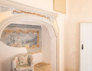 Une pièce avec une porte blanche, un arc en plein cintre orné, également blanc, et une chaise à motifs floraux.