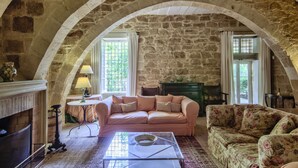 Une pièce chaleureuse avec un plafond voûté en pierre, une cheminée, un canapé rose et un fauteuil à motifs floraux.