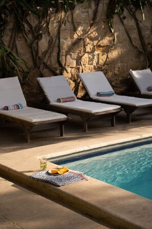 A poolside area with lounge chairs and a small table with a towel and fruit. - Luxurious Grand 18th C. Palace with Gardens & Pool (Ghaxaq)