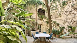 Une cour avec une table ronde et des chaises, entourée de plantes en pot et d’un mur de pierre.
