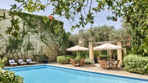 Une piscine entourée de verdure et d’un mur de pierre, avec des chaises longues et des parasols.