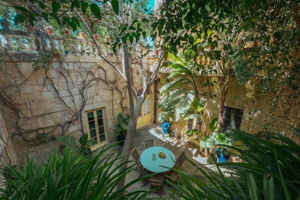 A courtyard with a round table and chairs, surrounded by stone walls and greenery. - Luxurious Grand 18th C. Palace with Gardens & Pool (Ghaxaq)