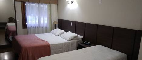A hotel room with two beds, a bedside table with a phone, a lamp, and a window with curtains.