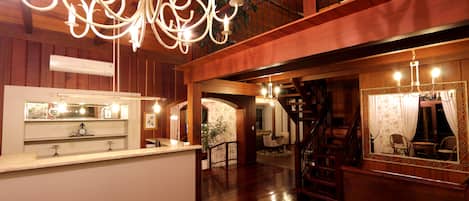 A spacious lobby with a wooden floor, a reception desk, a staircase, and a large chandelier.