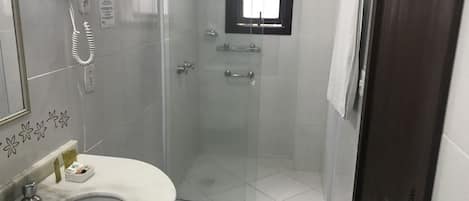 A bathroom with a sink, a hairdryer, a glass shower enclosure, and a small window.