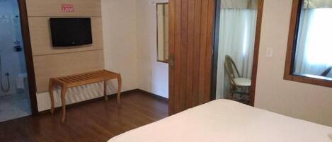 Una habitación de hotel con una cama, un banco de madera, un televisor montado en la pared y un espejo.
