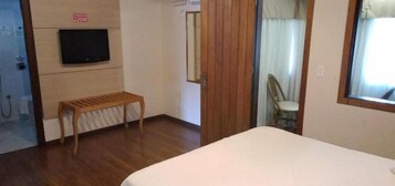 A hotel room with a bed, a wooden bench, a TV mounted on the wall, and a mirror.
