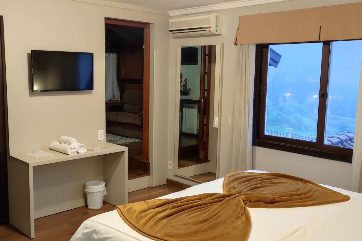 Habitación de hotel con cama, escritorio con espejo, televisión, armario y ventana con cortinas.