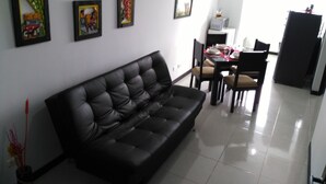 A modern living room with a black leather sofa, a dining table set for four, and three framed artworks on the wall. - Apartamento Turístico Familiar (Montenegro)