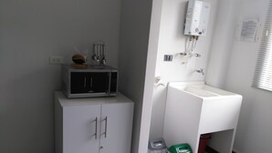 A small, clean bathroom with a white sink, a mirror, and a heater mounted on the wall. There is a cabinet with a microwave on top and two trash bins. - Apartamento Turístico Familiar (Montenegro)