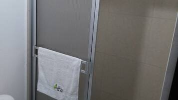 Un baño con inodoro, zona de ducha con puerta de cristal y un tapete azul en el suelo.