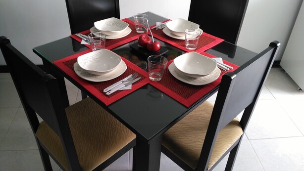 A dining table set with white plates, cutlery, and glasses, surrounded by black chairs with brown cushions. - Apartamento Turístico Familiar (Montenegro)