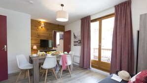 Una sala de estar moderna con sofá, mesa de comedor y sillas. Hay un televisor y una ventana con cortinas.