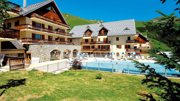 Un hotel de varios pisos con piscina, balcones y montañas al fondo.
