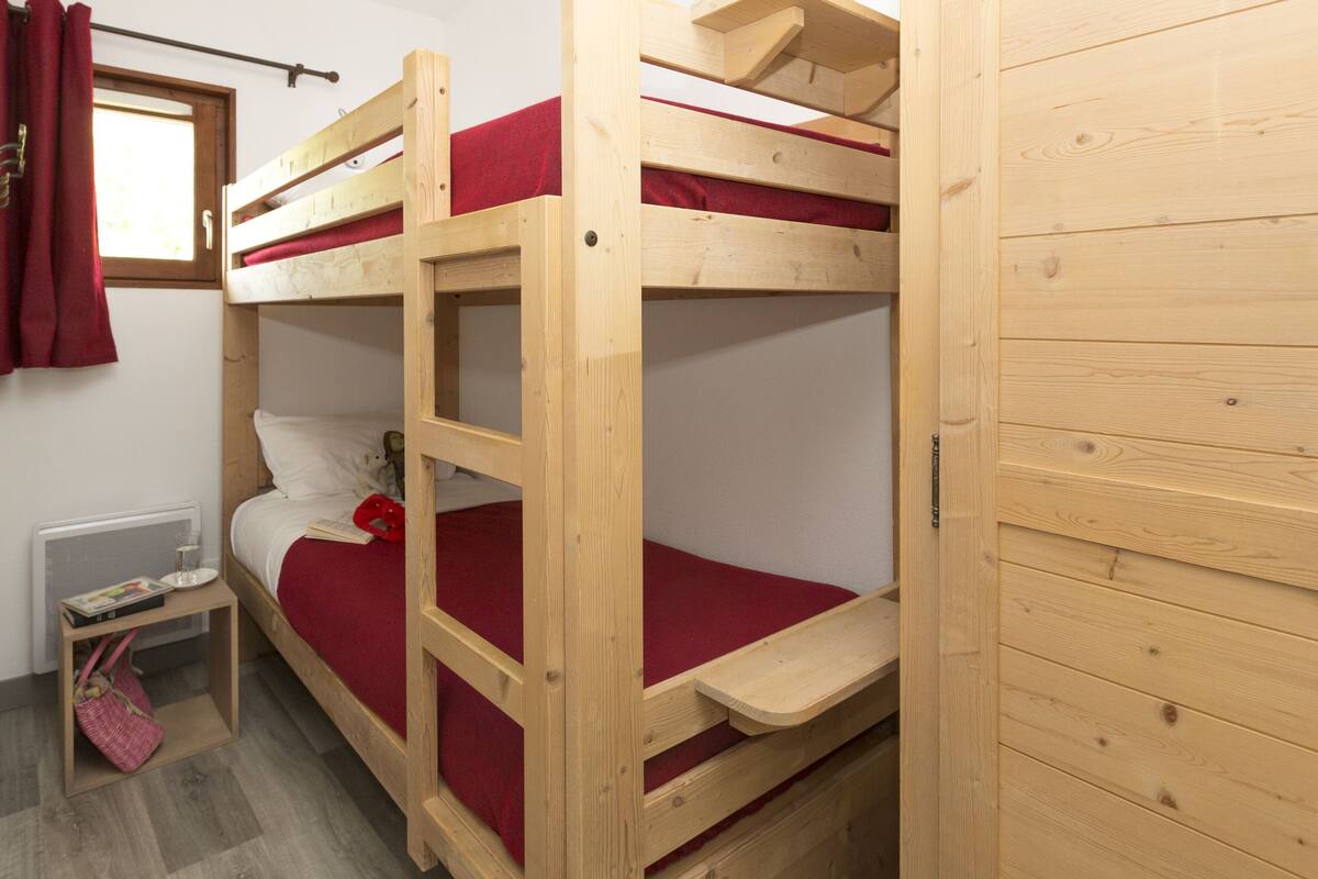 Une chambre avec un lit superposé, une petite table de chevet et une fenêtre avec des rideaux.