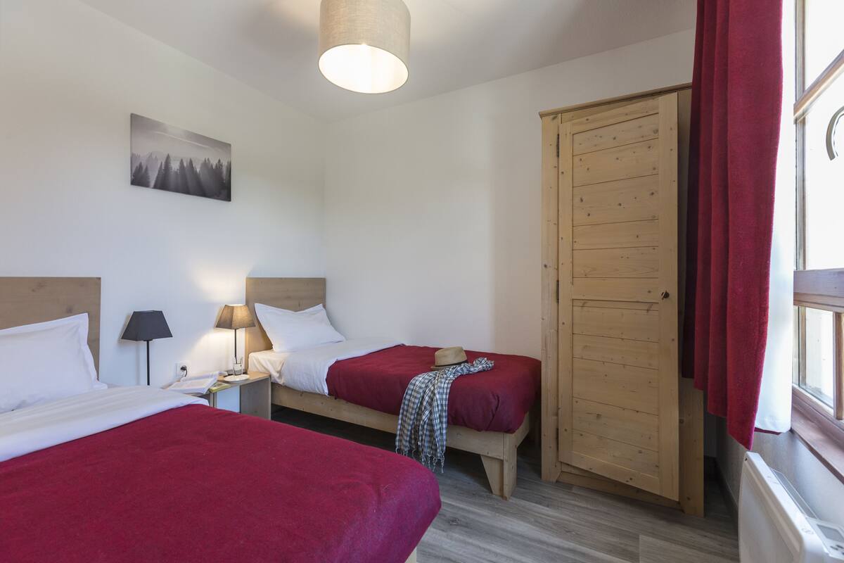 Une chambre d’hôtel avec deux lits, une armoire en bois, un tableau au mur et une fenêtre avec des rideaux.