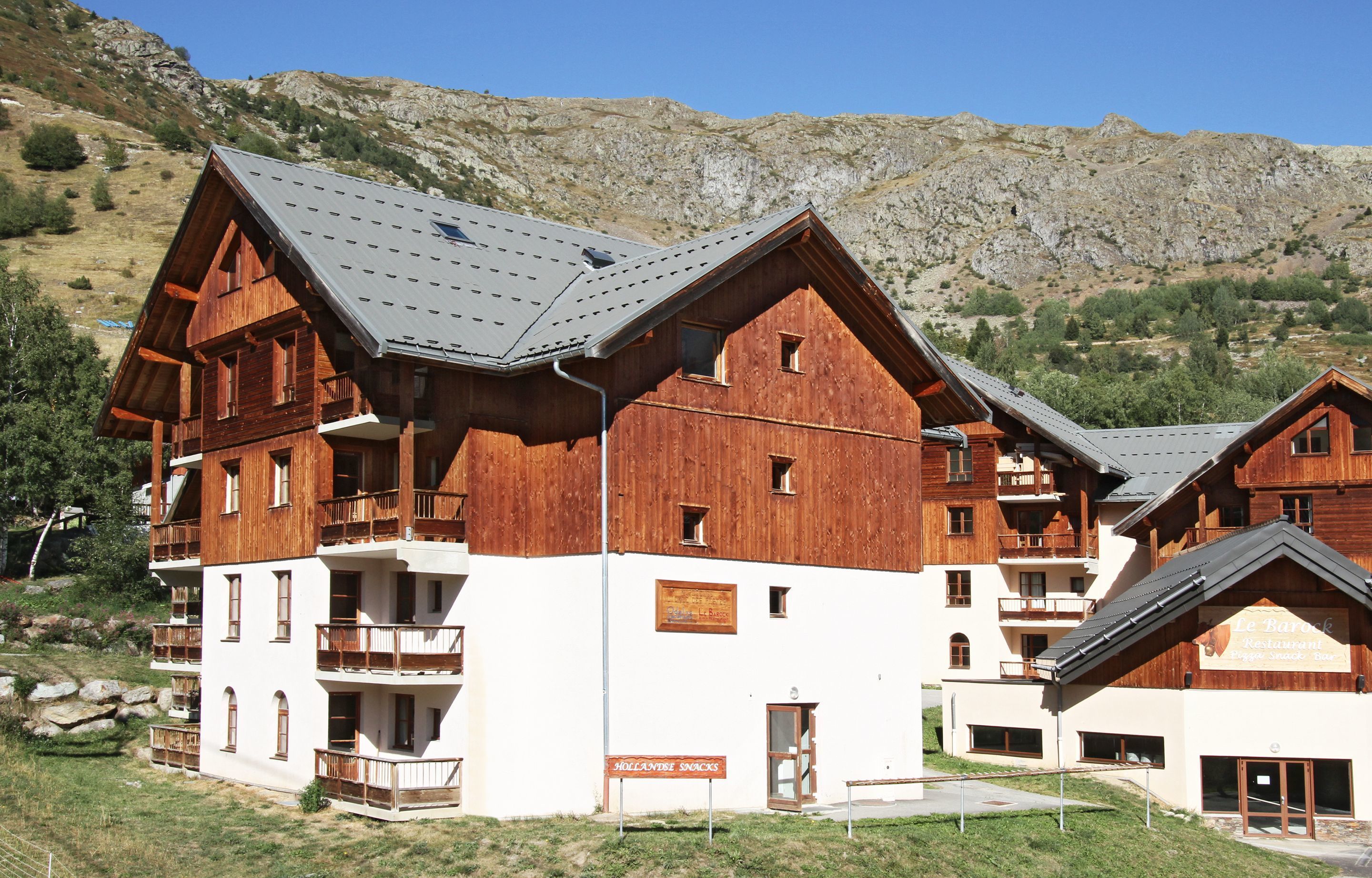 Un edificio de madera de varios pisos con balcones, un letrero que dice 'Jollansite Snacks' y un paisaje montañoso al fondo.