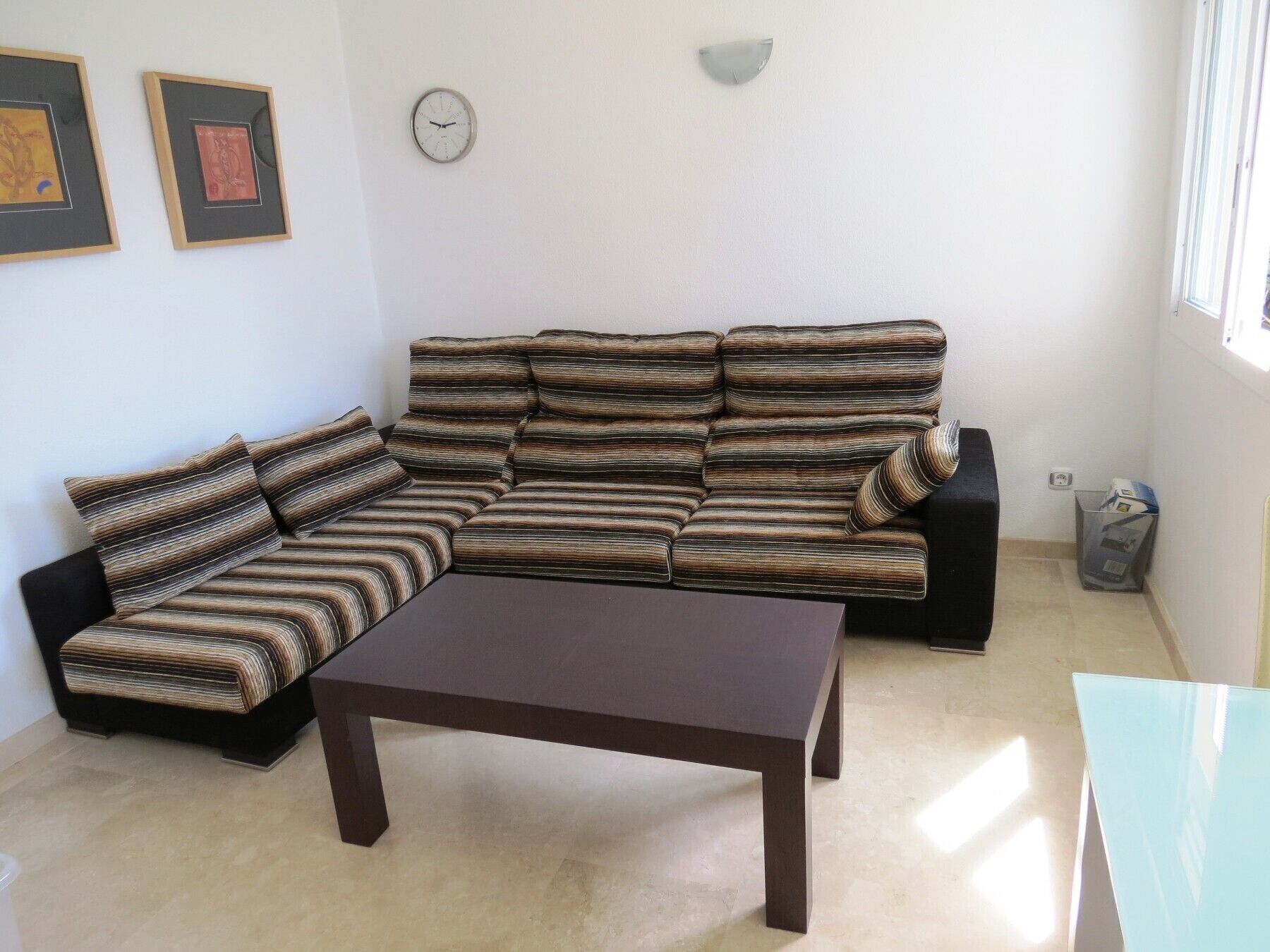A living room with a sectional sofa, a coffee table, a wall clock, and framed artwork.