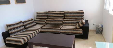 A living room with a sectional sofa, a coffee table, a wall clock, and framed artwork.
